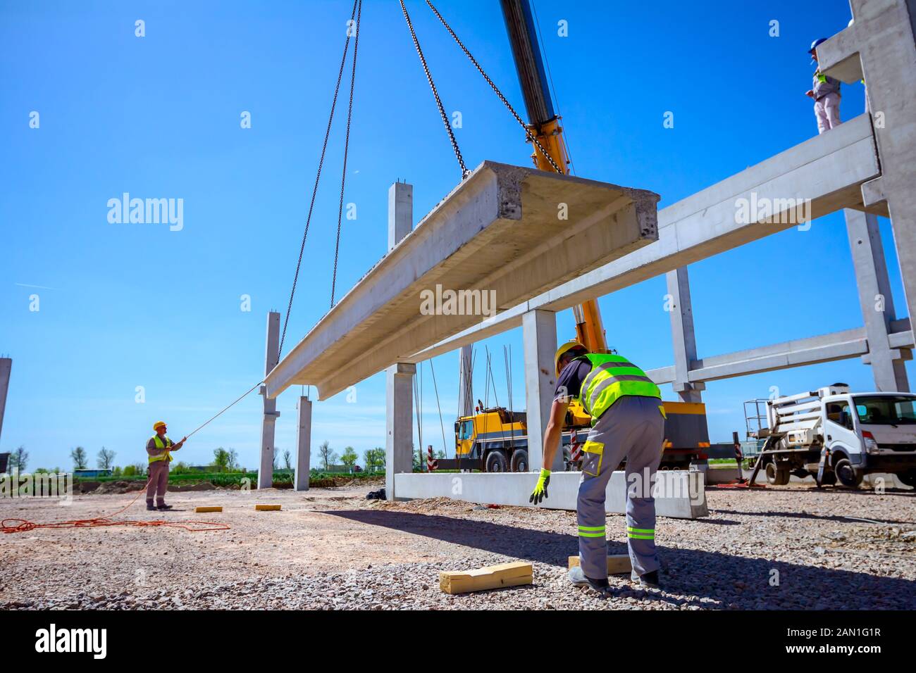 Workers are helping mobile crane to manage concrete joist for assembly ...