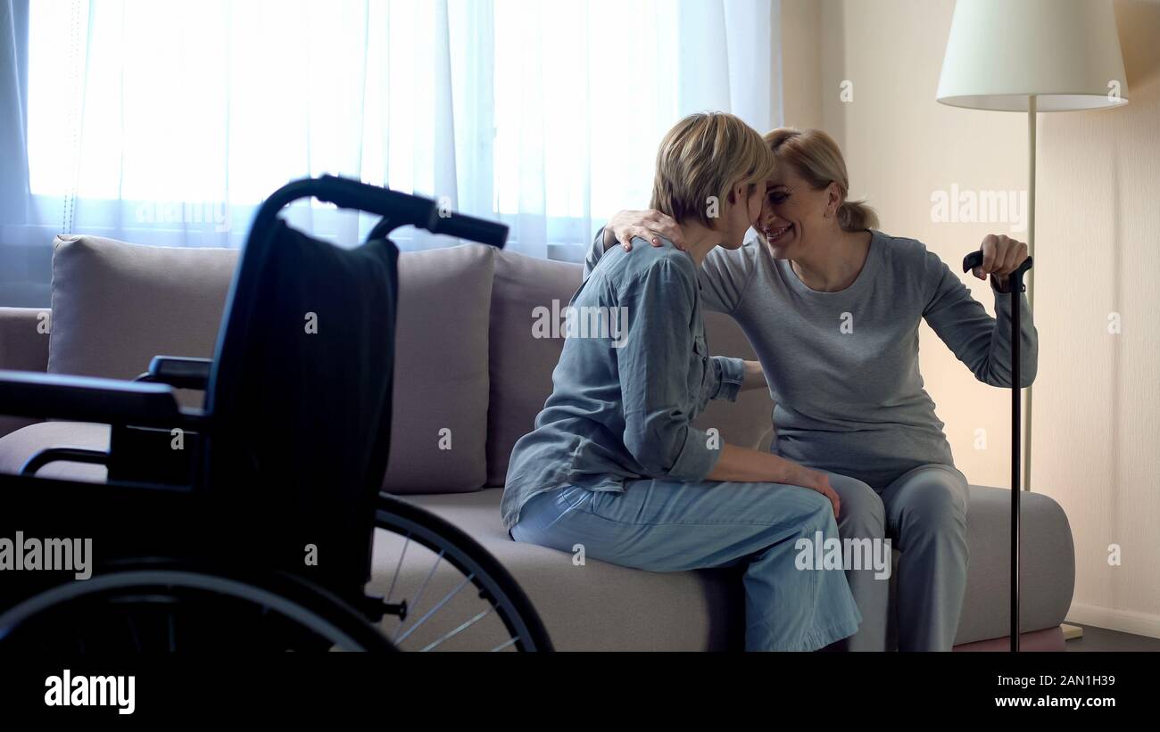 Disabled mother sitting on couch and talking to daughter, family