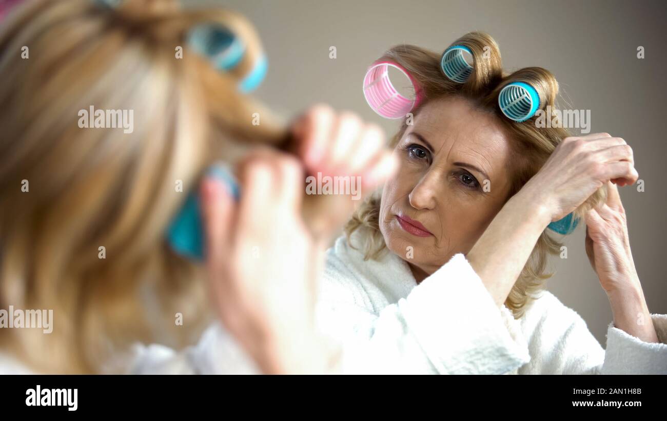 Retired female fixing hair curlers and preparing for romantic date, appearance Stock Photo
