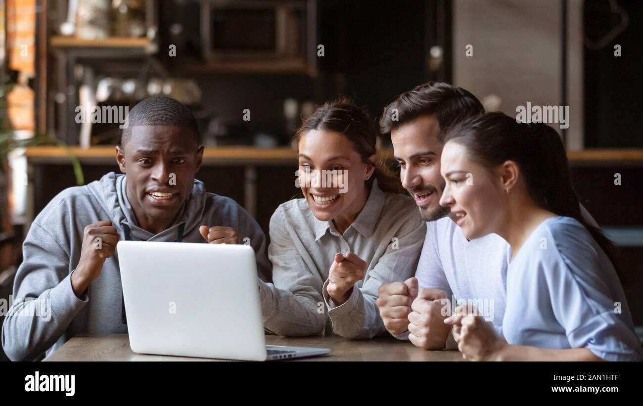 Excited diverse friends cheering watching match on laptop online Stock Photo