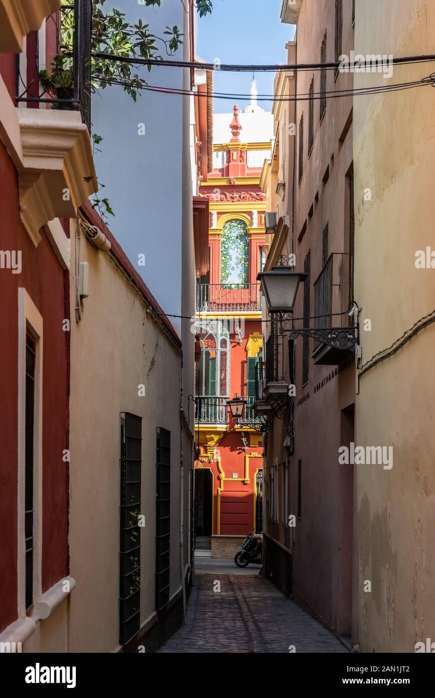A striking ochre building accented with bright yellow details and ceramic tiles at the end of a narrow alley leading on to Calle Aguilas in Seville Stock Photo