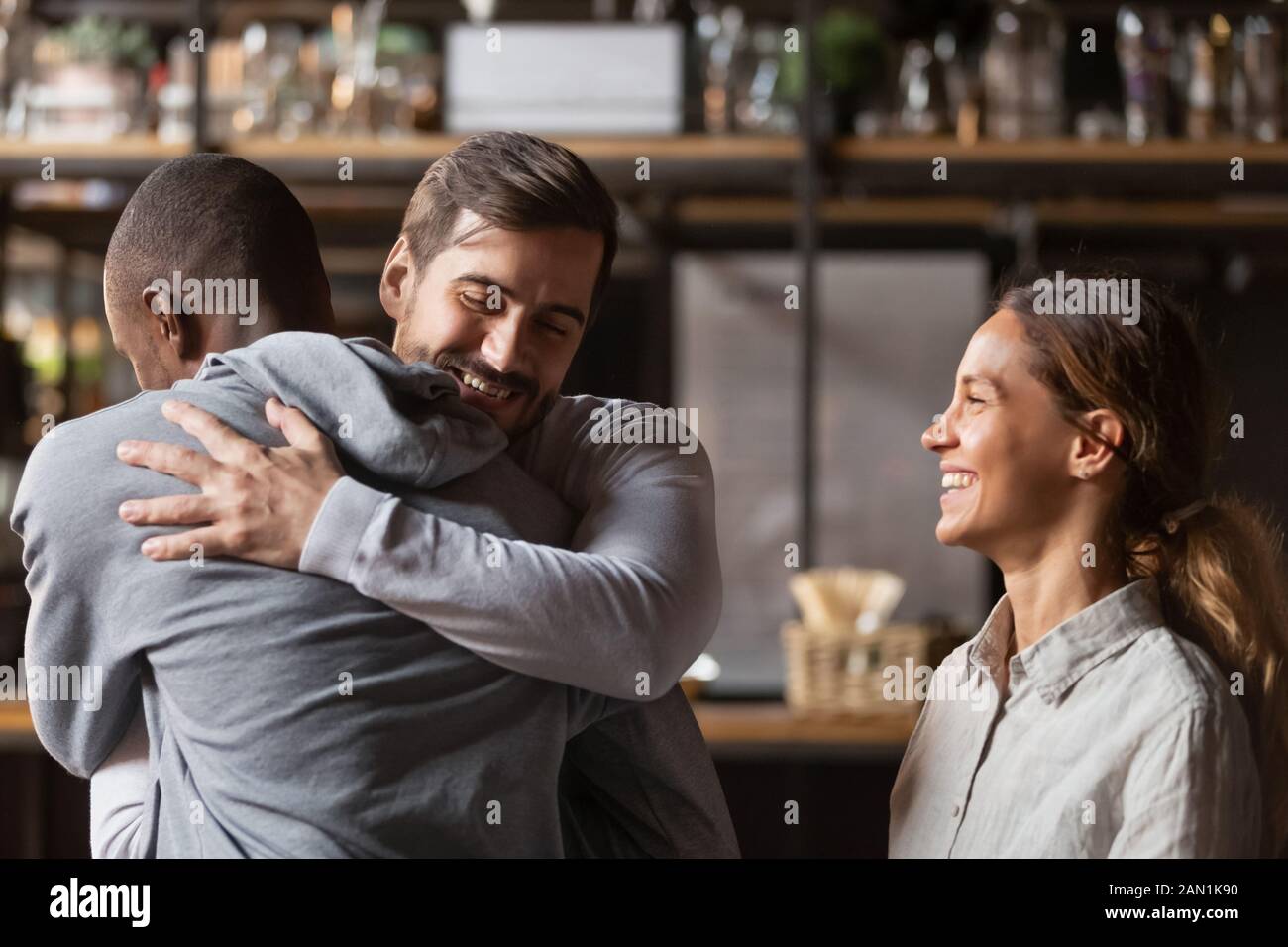 Overjoyed diverse friends embrace welcoming pal in bar Stock Photo