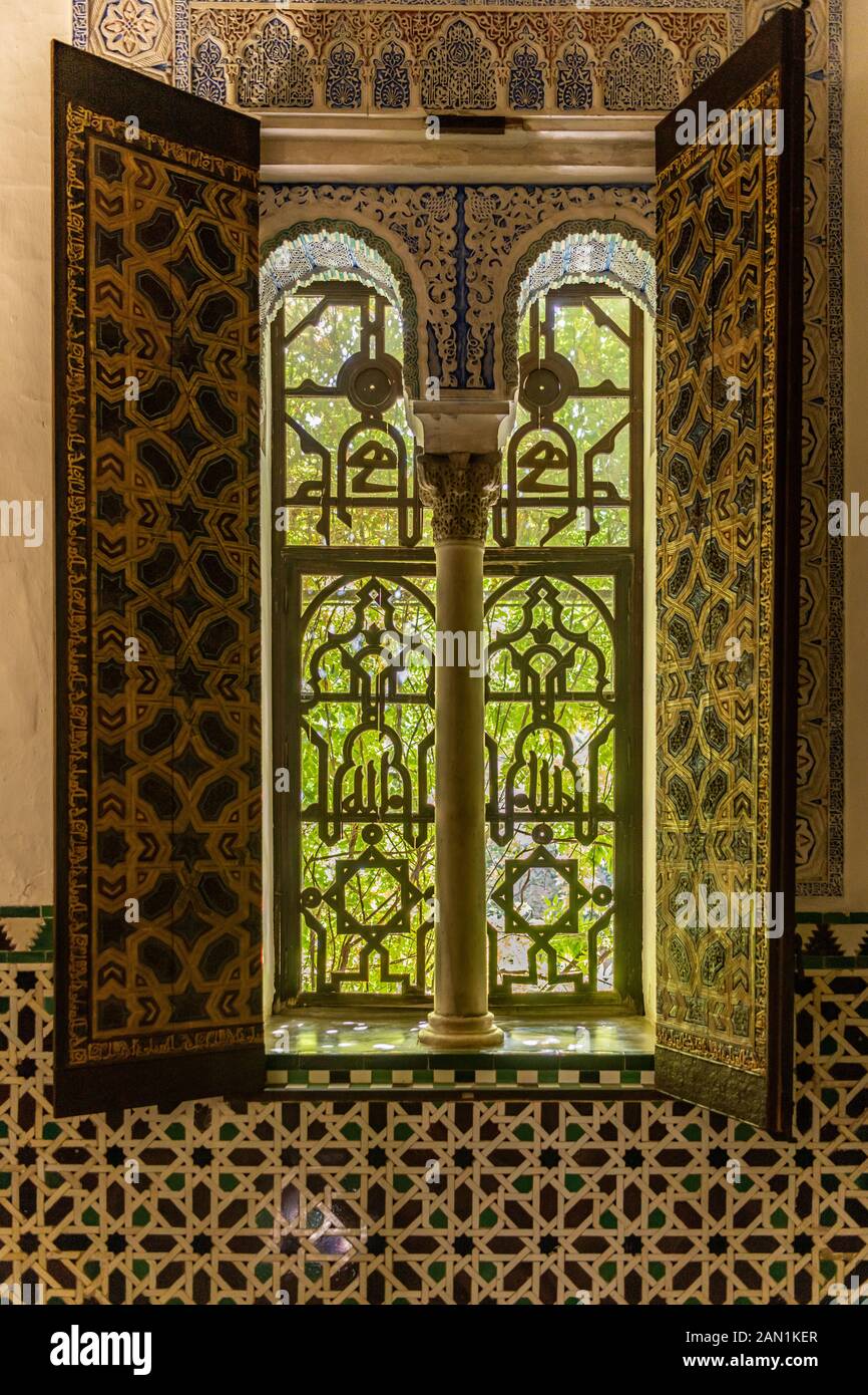 Decorated shutters frame a highly ornate arched window into the Alcazar Palace garden. Stock Photo
