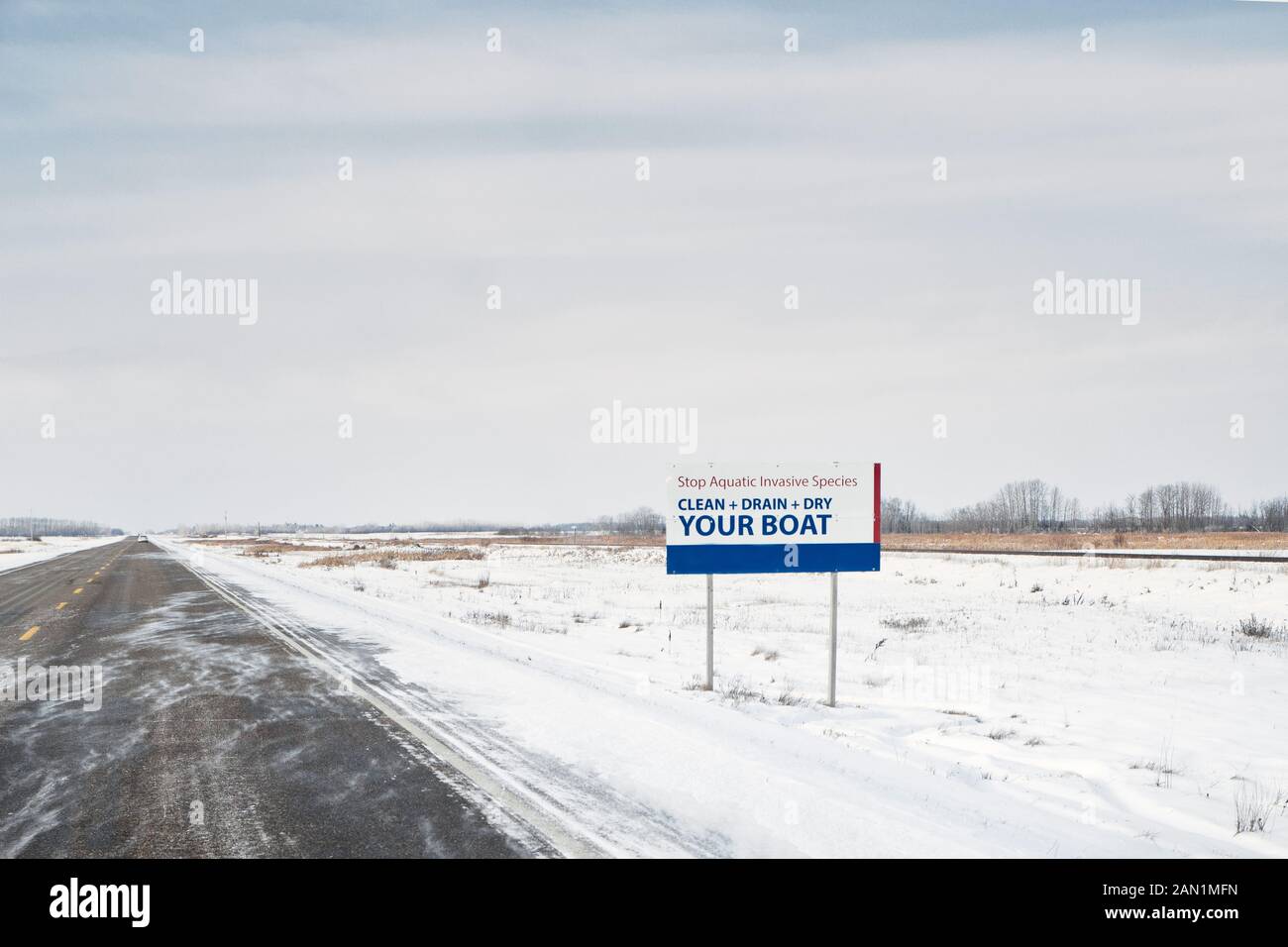 An advertisement reminding you to clean, drain and dry your boat along a deserted highway in a blustery prairie winter landscape Stock Photo