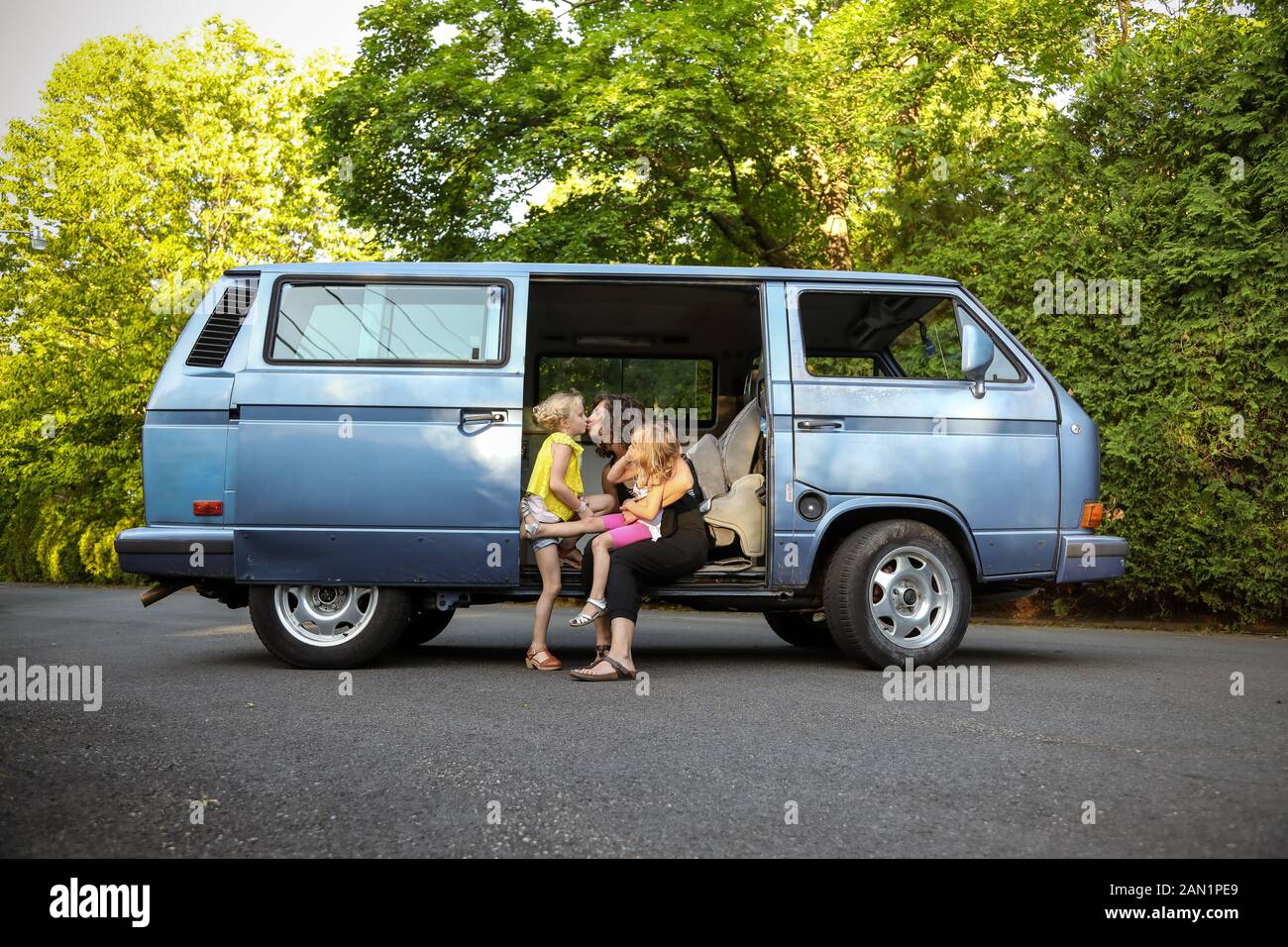 little girls and mom sitting in doorway of vintage van giving a kiss Stock Photo