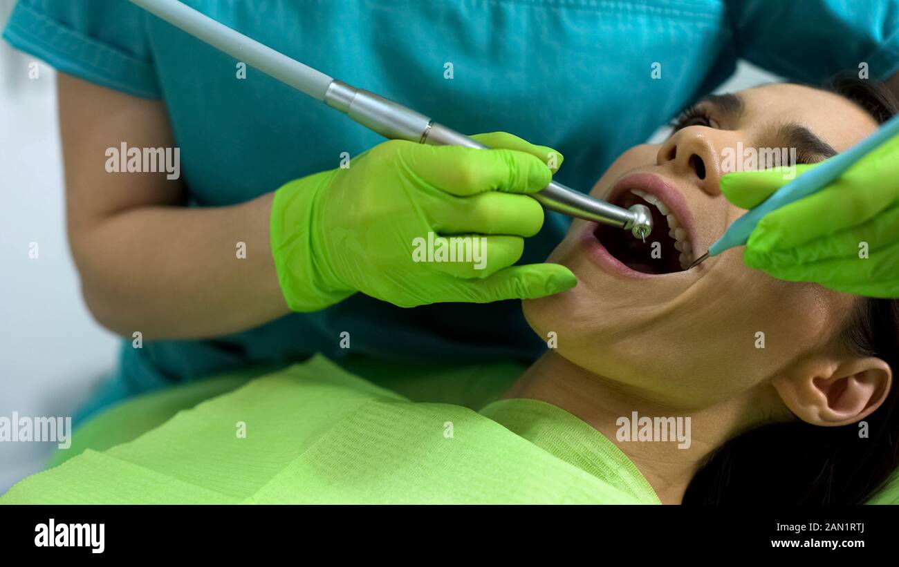 Female dentist using dental drill to treat patient teeth, modern