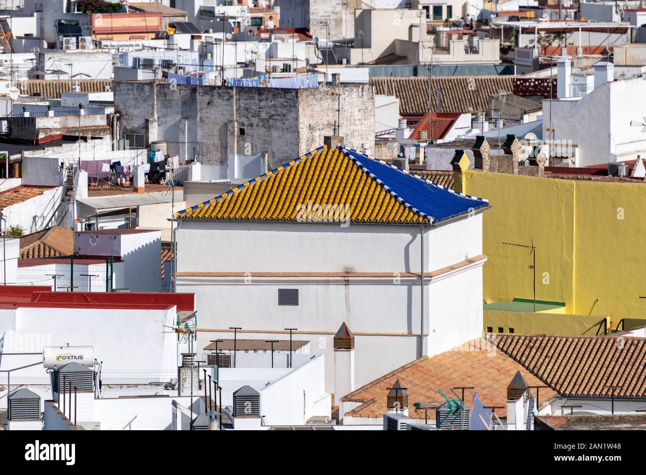 A vibrant blue and ochre ceramic tiled roof tops a white tower of a building on Calle Amparo in Seville. Stock Photo