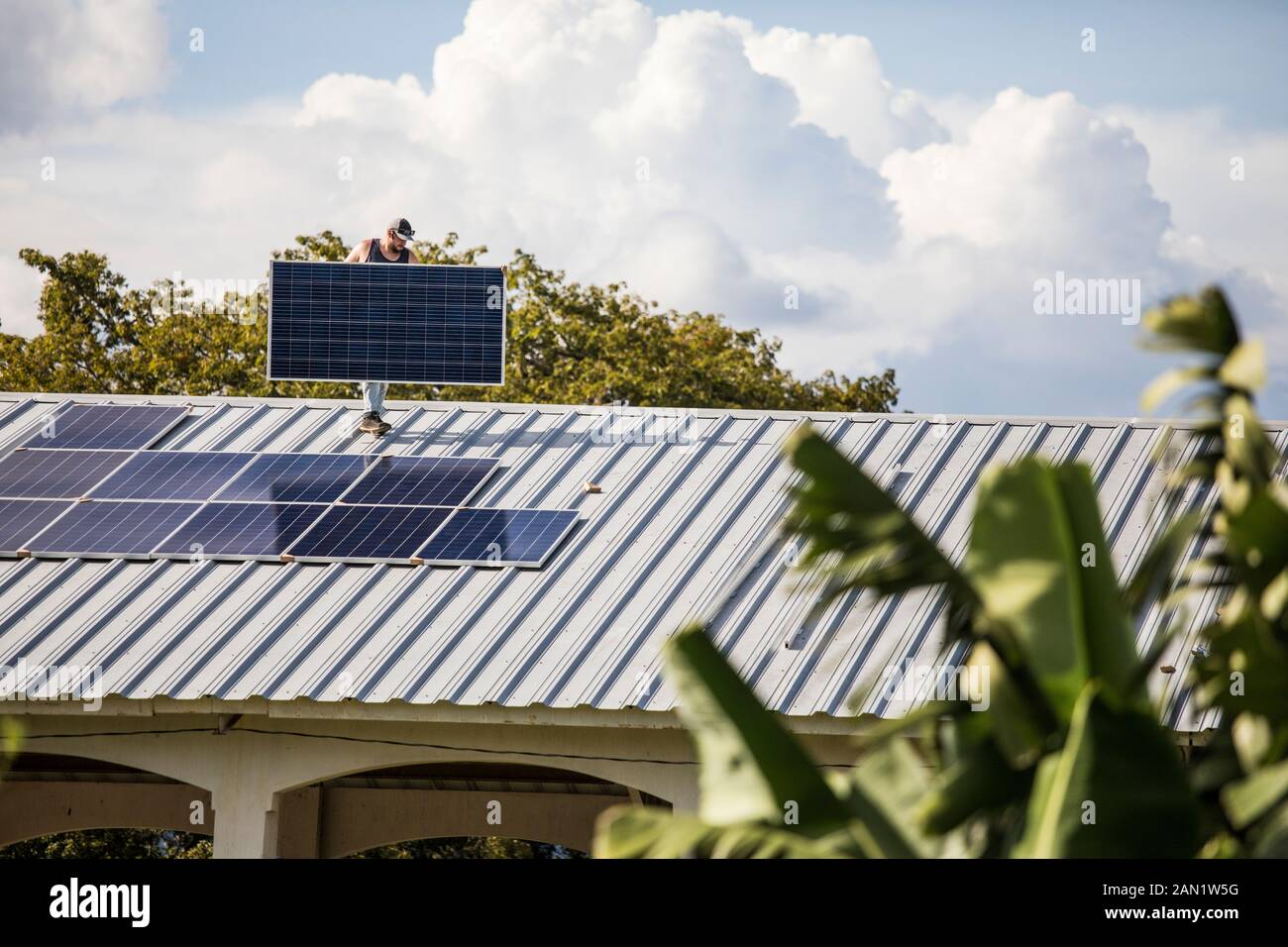 Construction worker carries solar panel on rooftop during install. Stock Photo