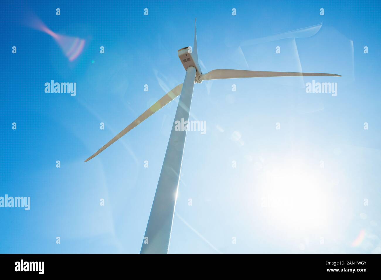 Looking up at wind turbine against blue sky with sun flare Stock Photo