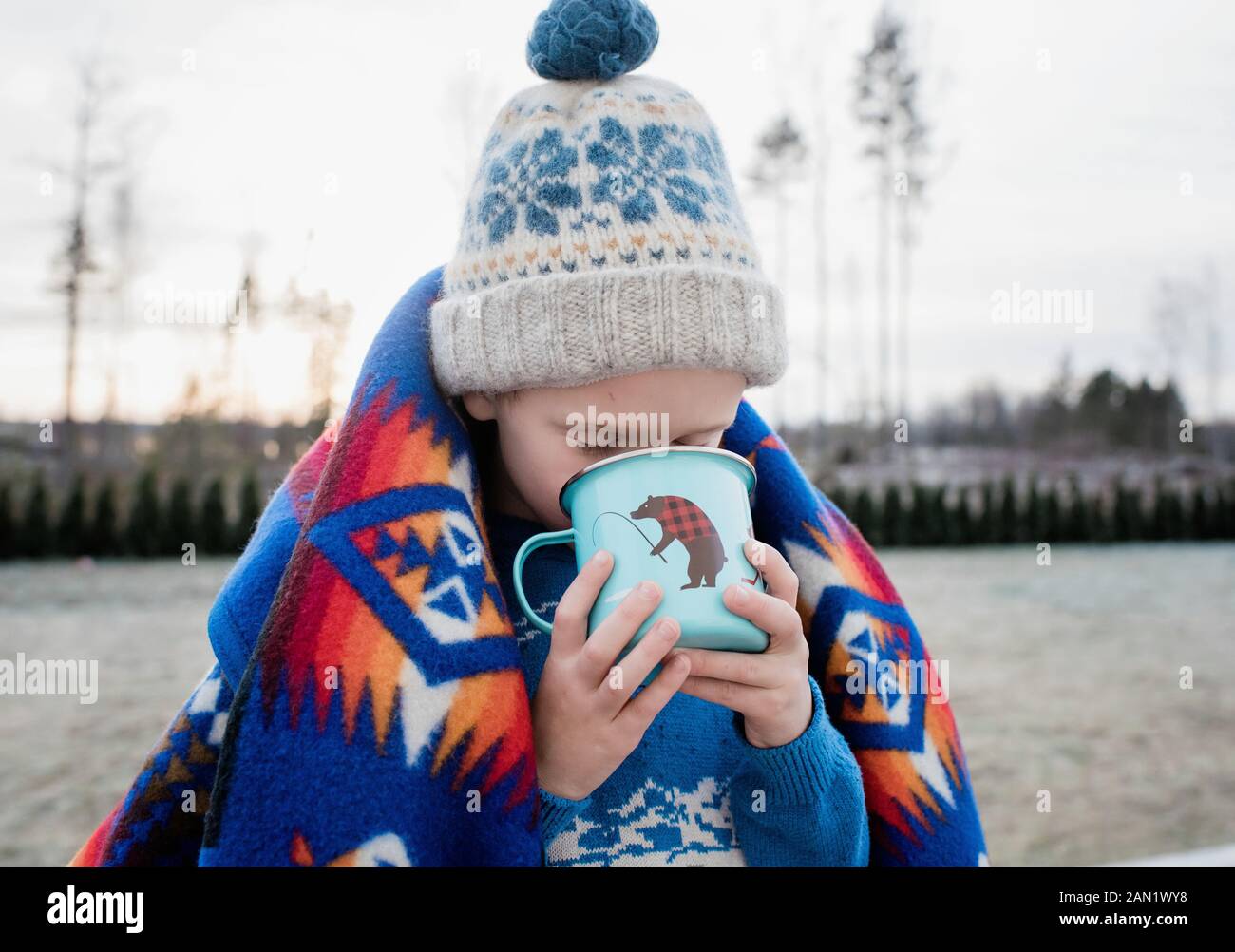 young boy wrapped in a blanket drinking hot chocolate outside Stock Photo