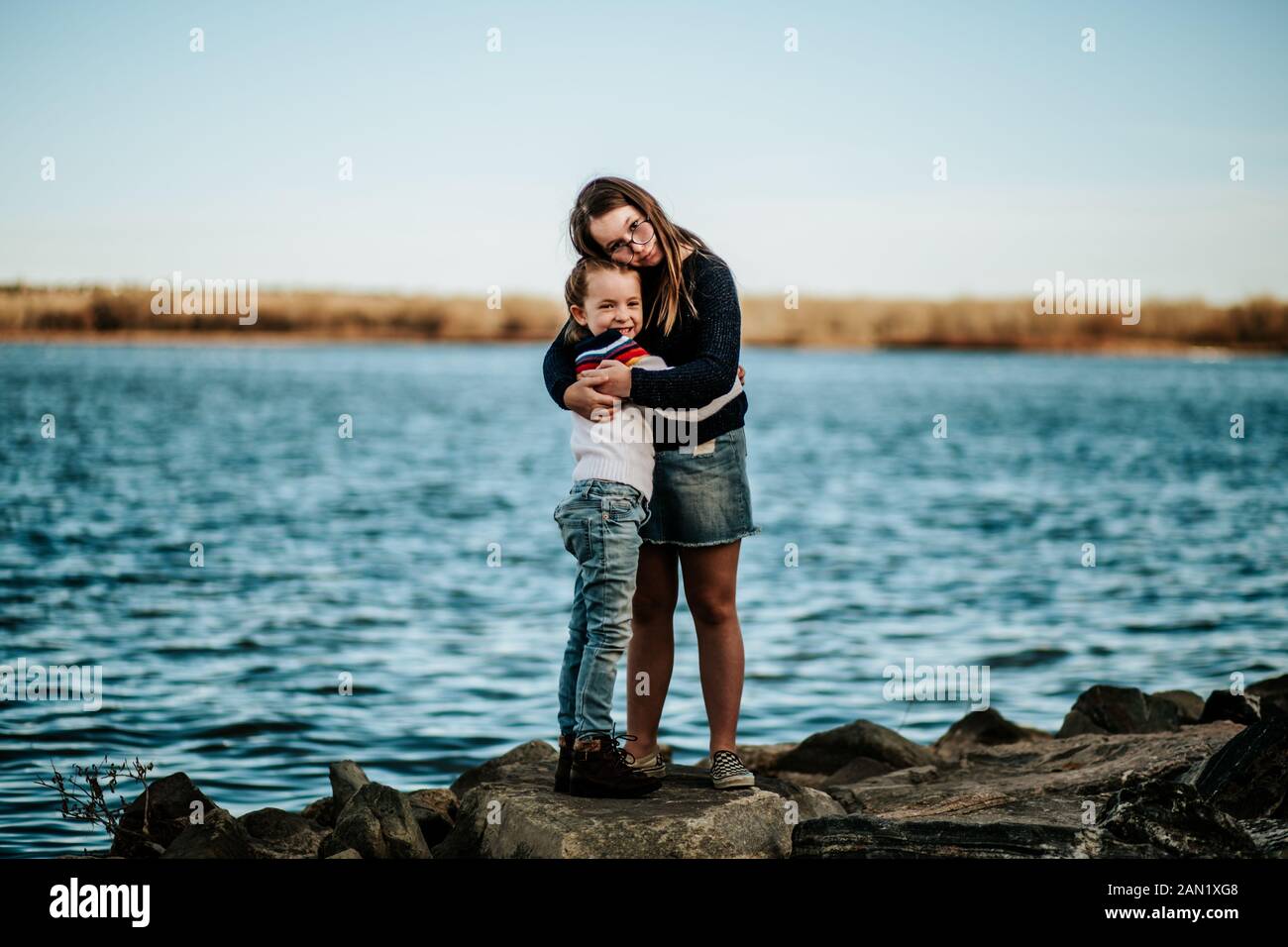 Portrait of sisters hugging on a rock near a lake Stock Photo
