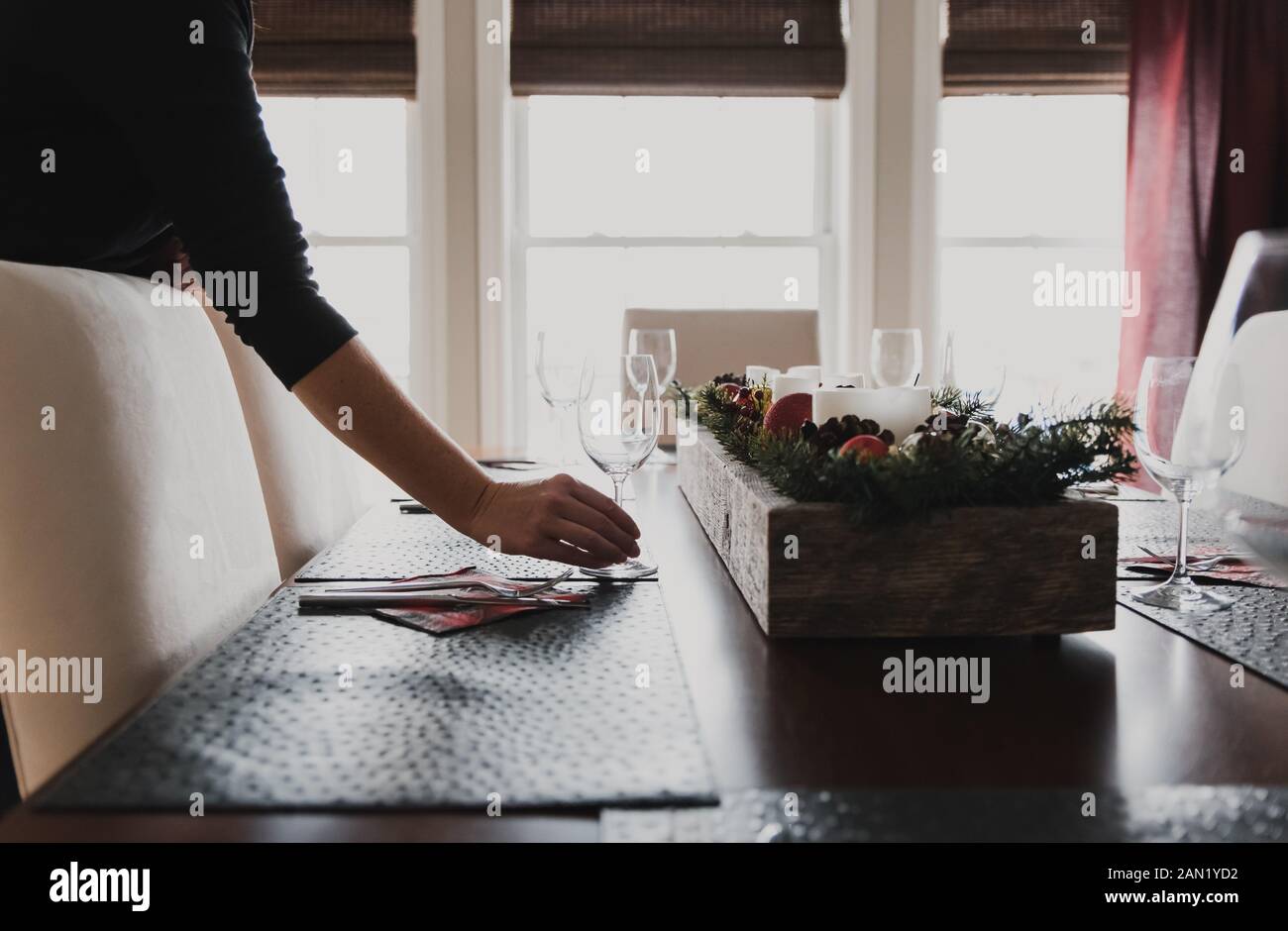 Close up of hand placing wine glass on place setting of dining table. Stock Photo