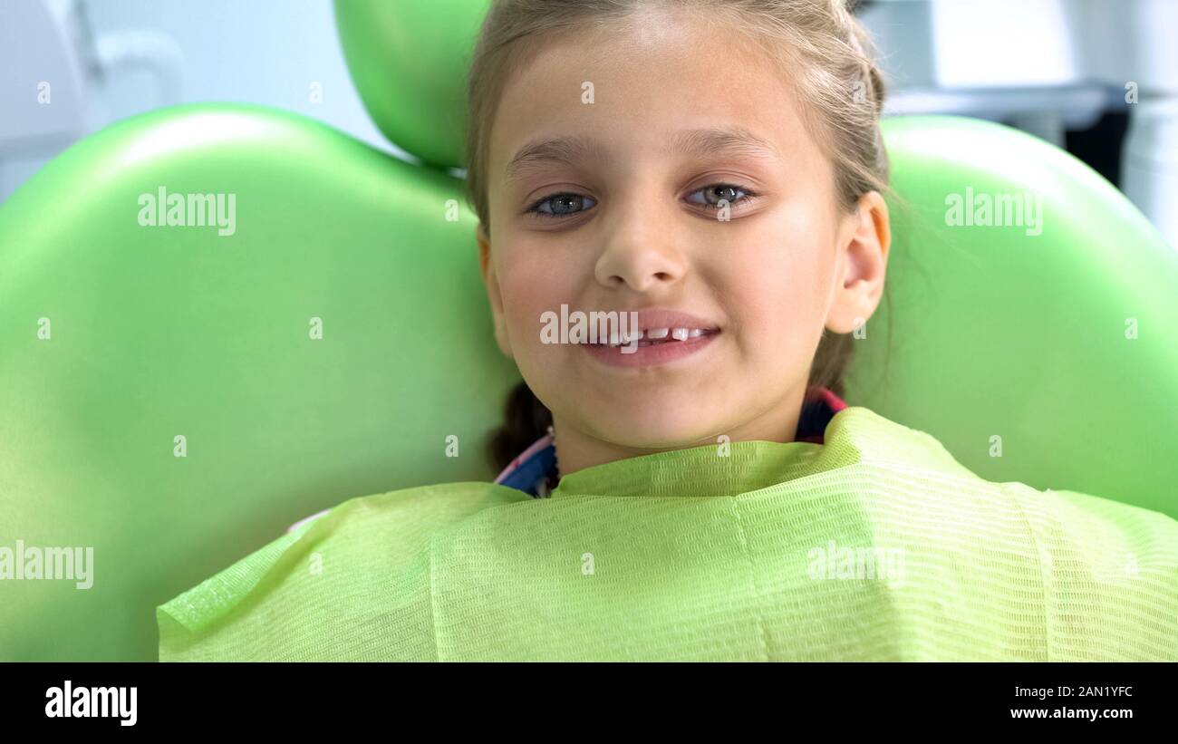 Little smiling girl sitting in dentist chair after procedure, oral