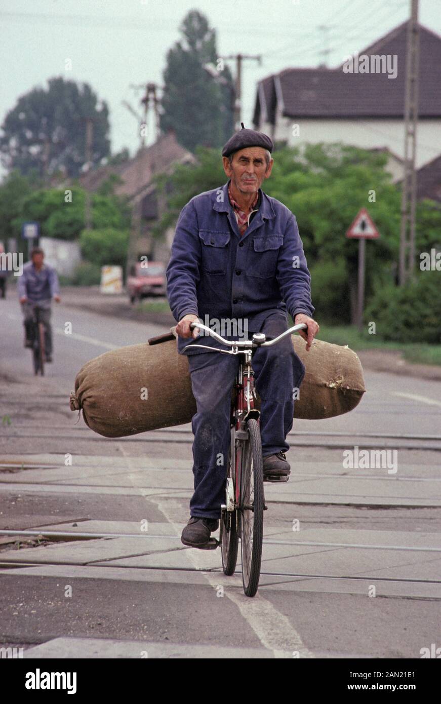 A Hungarian man cycles on the road with a large sack of produce  in a village in rural Hungary, on 18th June 1990, in Hungary. Stock Photo