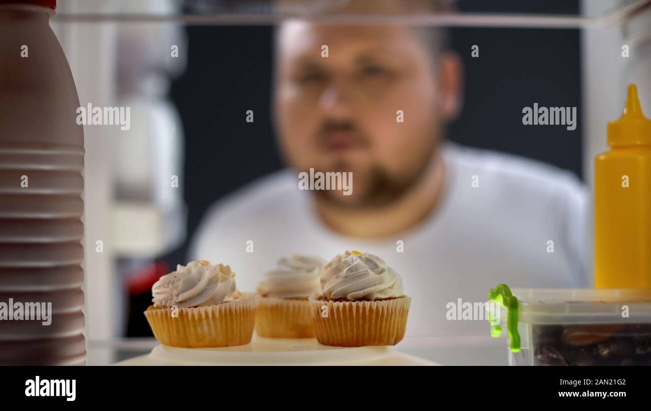 Hungry fat man looking at cream cakes in fridge at night, diabetes risk,  sugar Stock Photo - Alamy