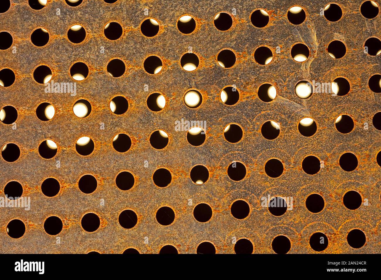 perforated metal with circular holes mostly black, some with translucent white light Stock Photo
