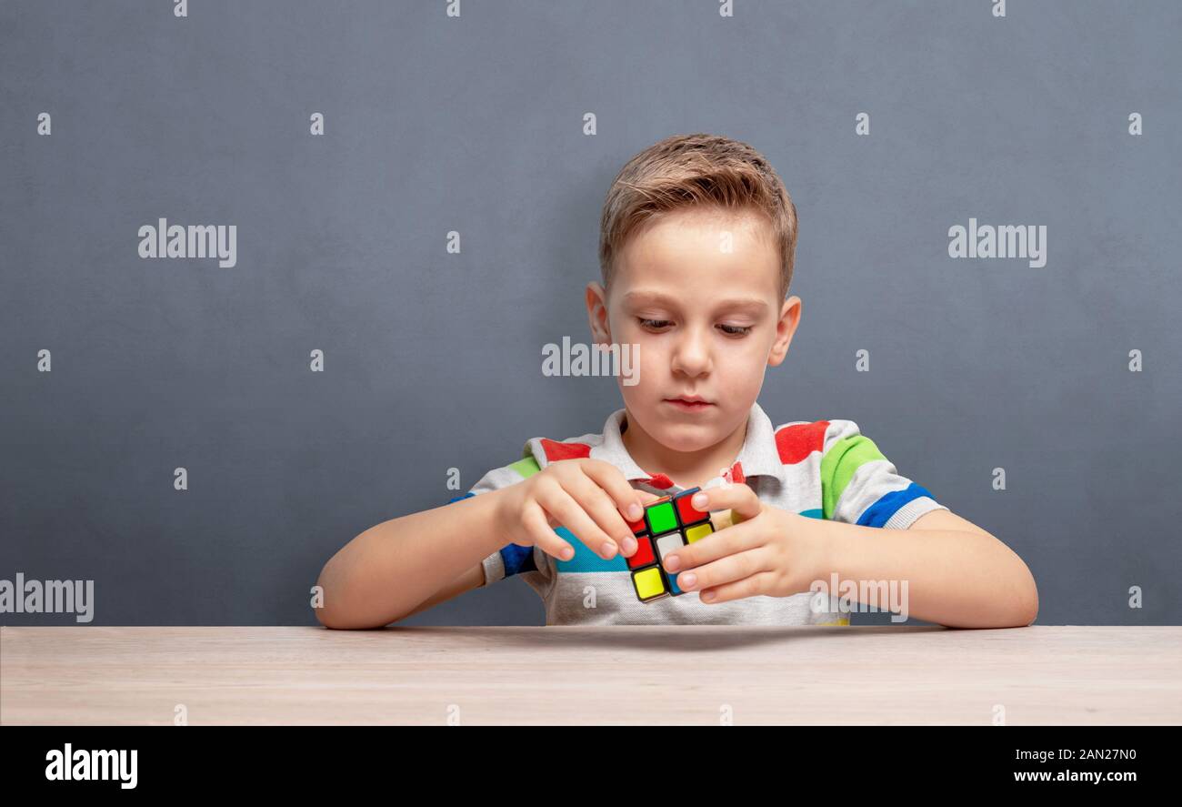 Boy assembles a rubik's cube. Concept of logic development and children self-confidence. Copy space on wall Stock Photo
