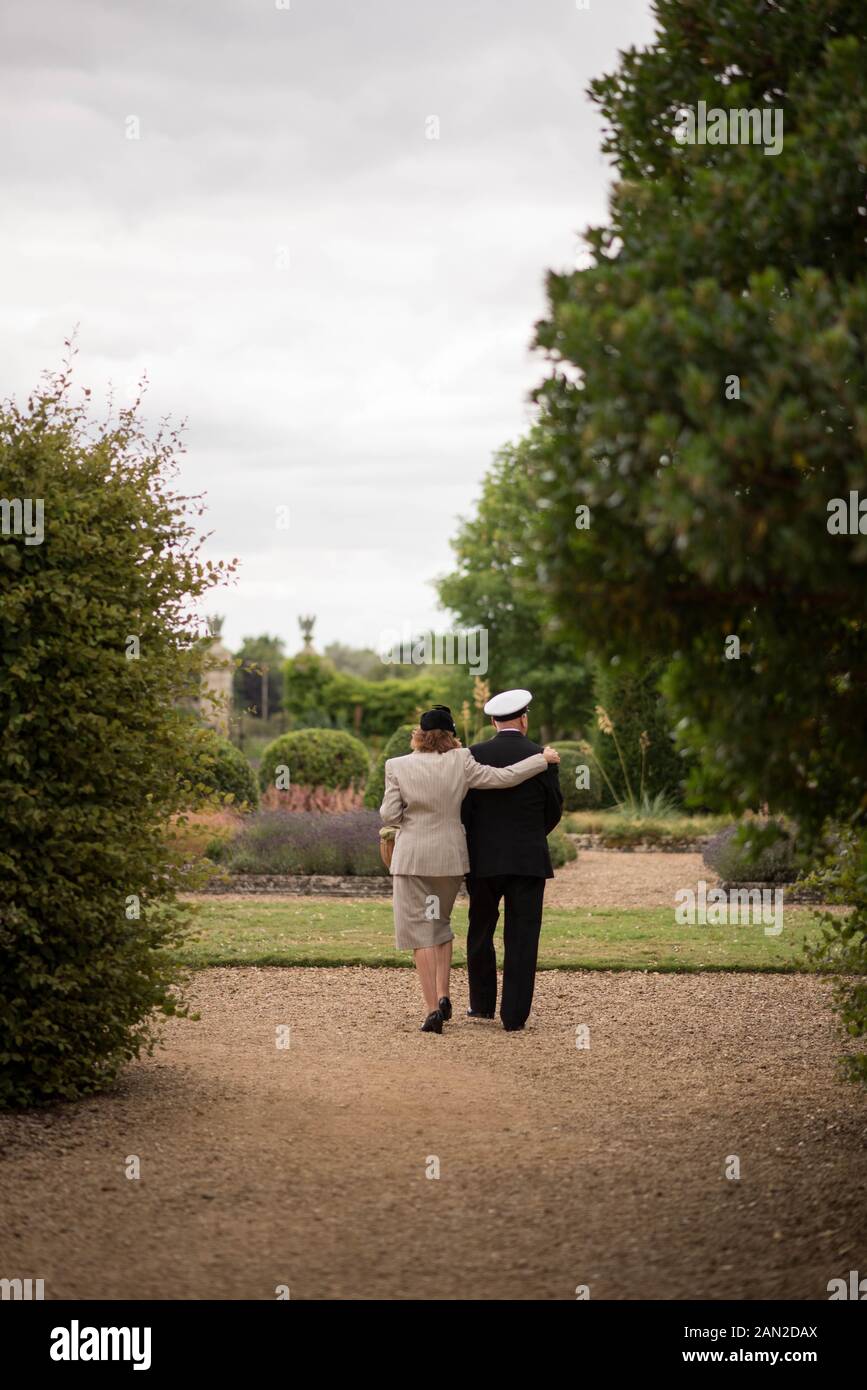 Couple walking away from camera in garden wearing World War 2 costume outfits in the gardens of Thorpe Hall, Peterborough Stock Photo