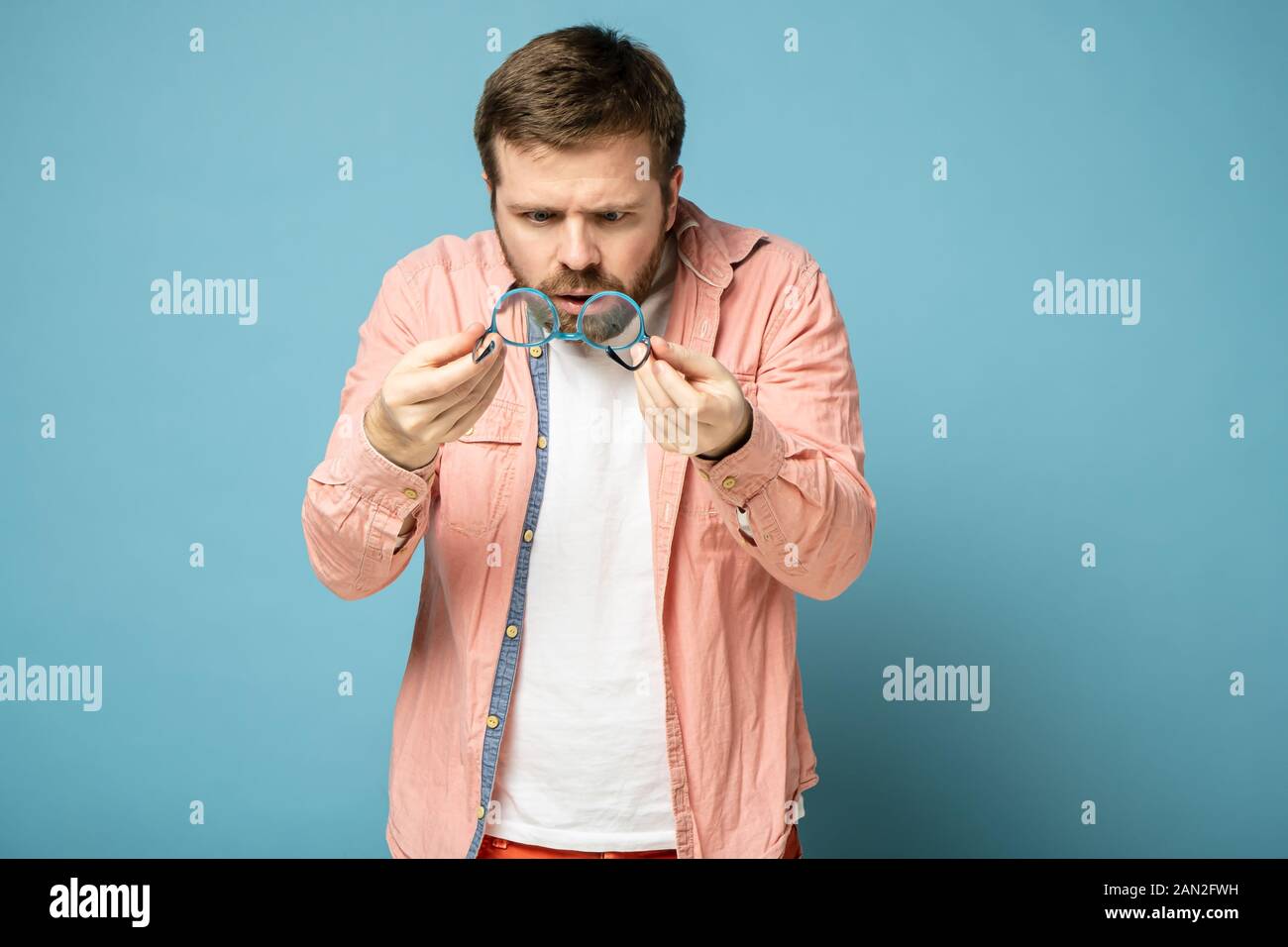 Shocked, strange bearded man holds glasses in hands and anxiously examines a lens. Stock Photo