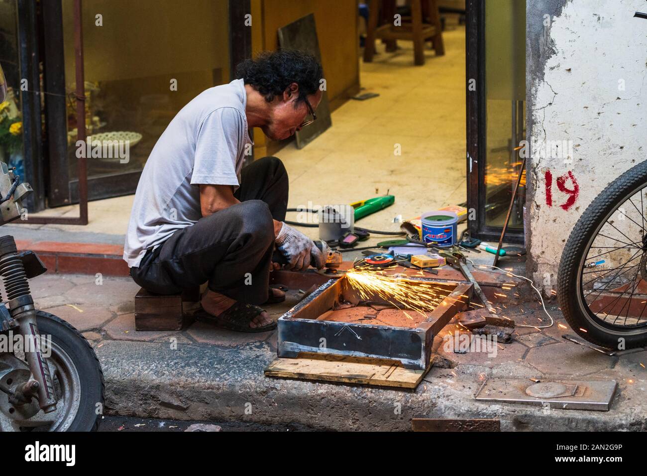 Hanoi, Vietnam - 18th October 2019: An old asian man repairs some metal on the street without any safety clothing or goggles Stock Photo