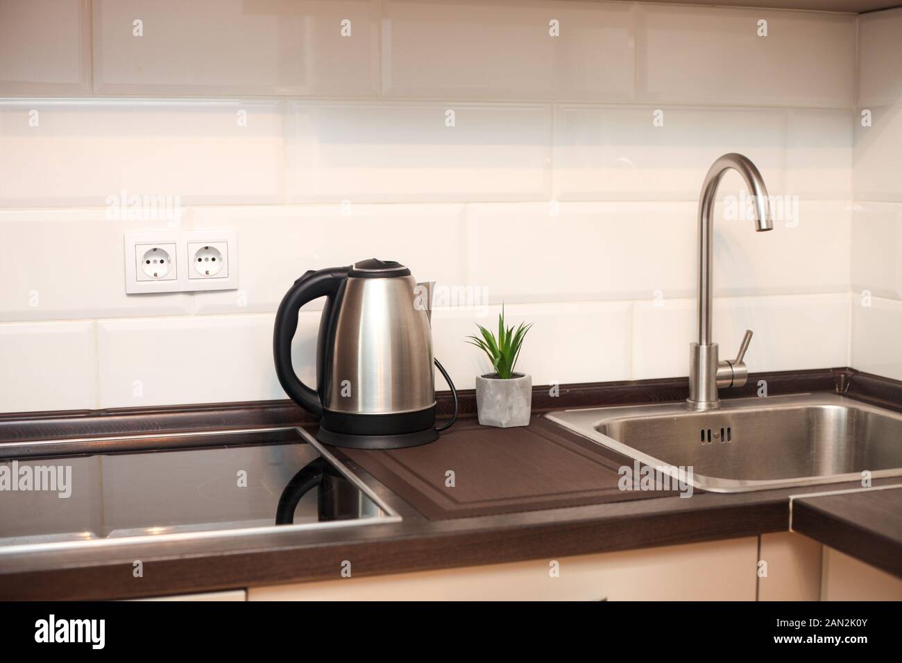 Modern kitchen with metal sink, kettle and white decorative wall