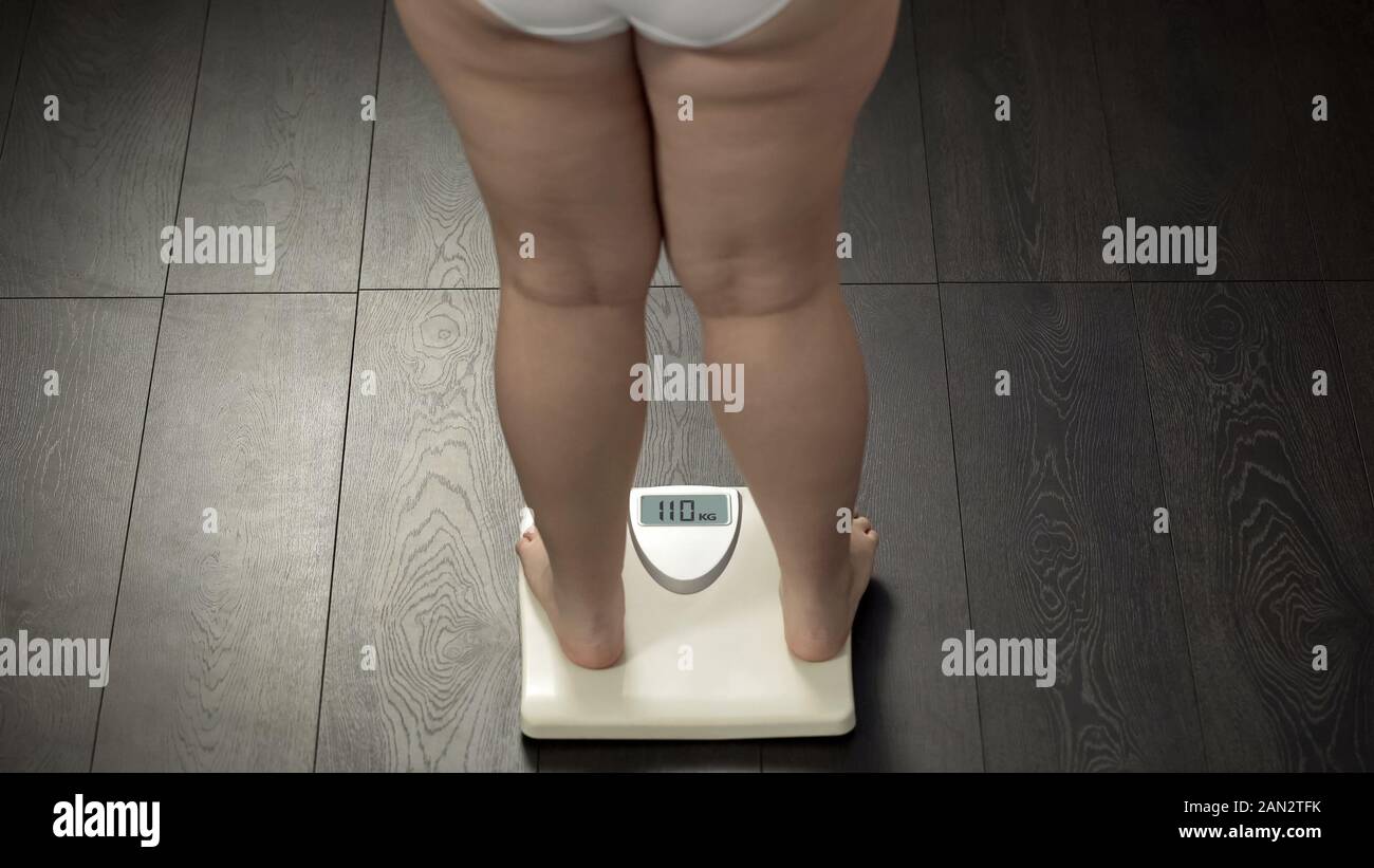 Obese female standing on bathroom scales to check body weight, fat