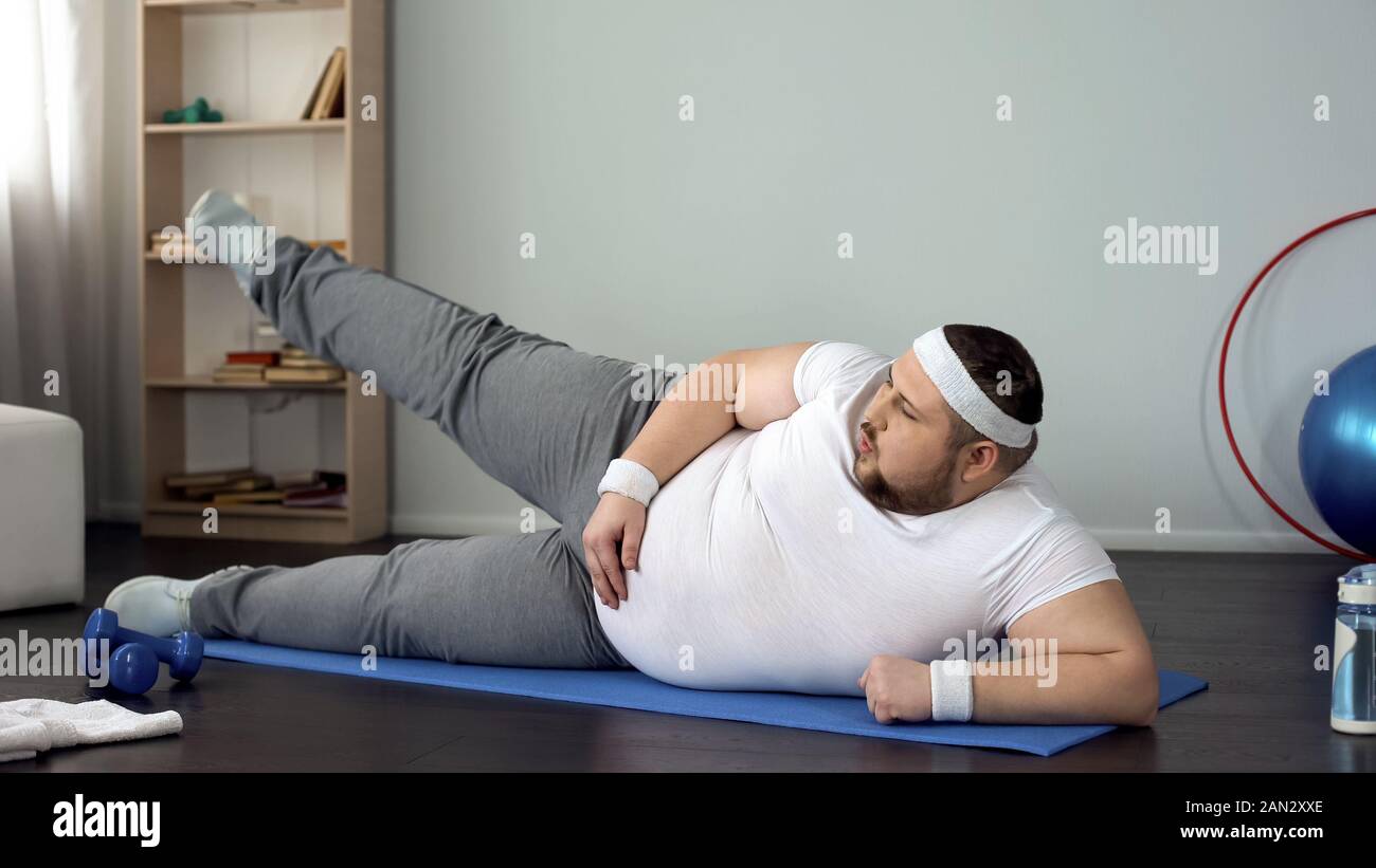 Obese male lifting leg lying on mat, healthy lifestyle, sport leisure, exercises Stock Photo