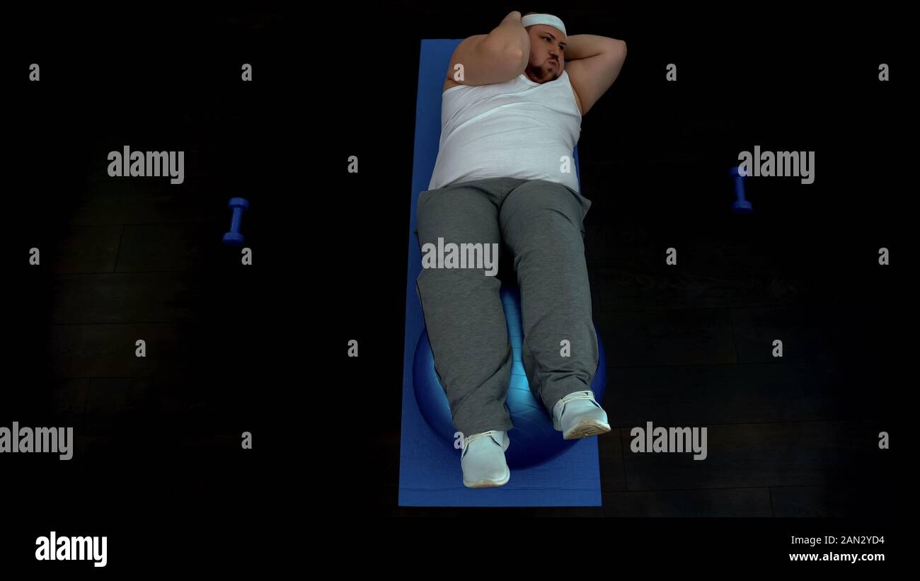 Fat man doing crunches on mat, abdominal exercises with fit ball, home