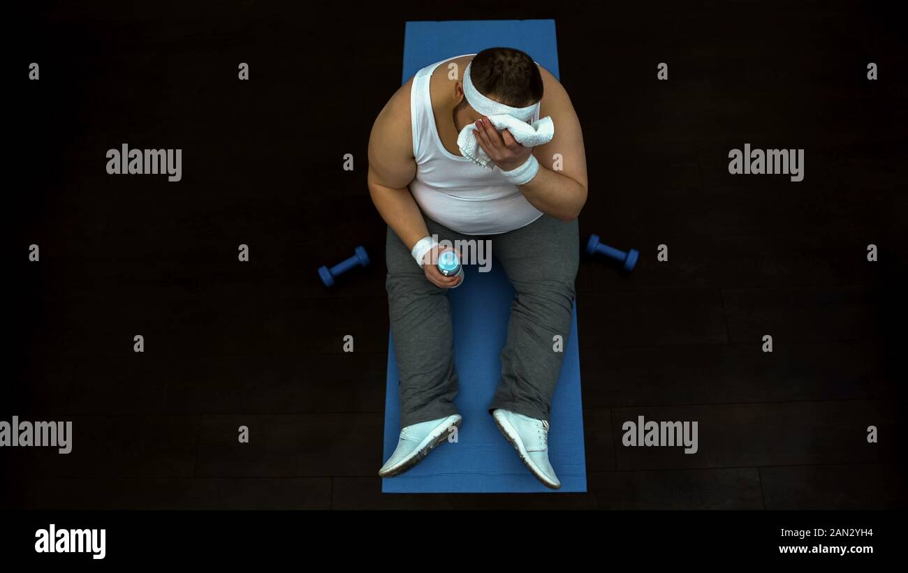 Overweight man wiping sweat from his forehead after exhausted training at gym Stock Photo