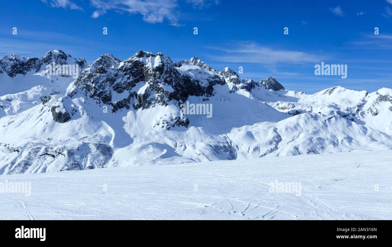 Alpine snowy peaks panorama with slopes, off piste on fresh powder in Zurs winter sport resort, Alps, Arlberg, Austria, on sunny cold day . Stock Photo