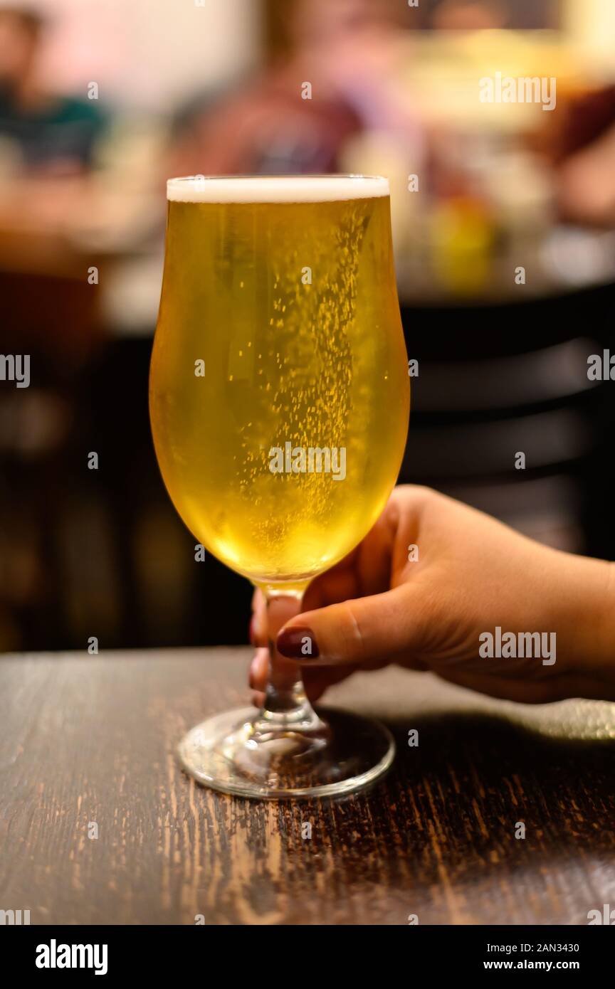 Hand holding misty glass with pint of cold yellow Scotch ale, pale ale