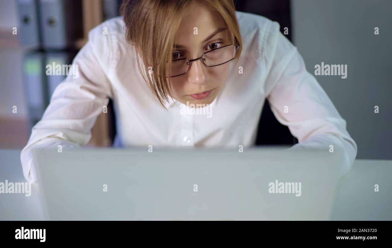 Tired secretary in eyeglasses attentively looking at computer screen, eye strain Stock Photo