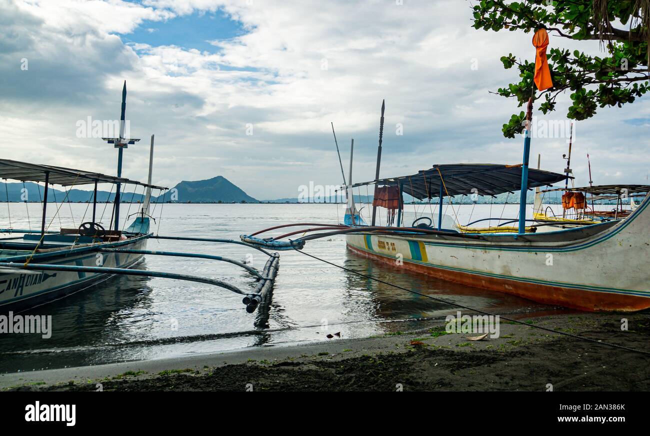 Outriggers on the shore of Taal lake in the Philippines with a view of the dormant Binintiang Malaki (Big Leg) volcano. Stock Photo