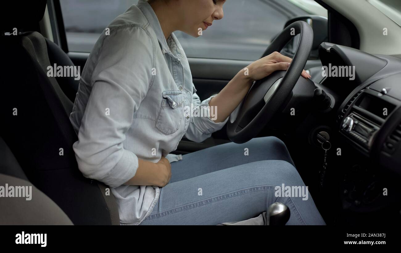 Woman in car feeling lower abdominal premenstrual pain, hormonal