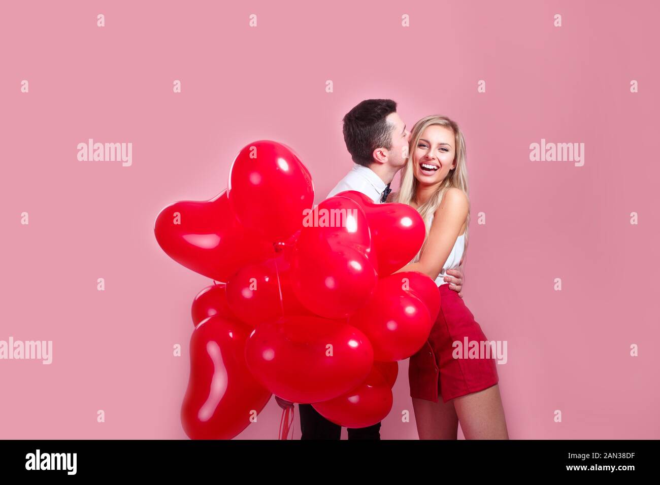 Happy kissing couple posing on pink background with balloons heart ...