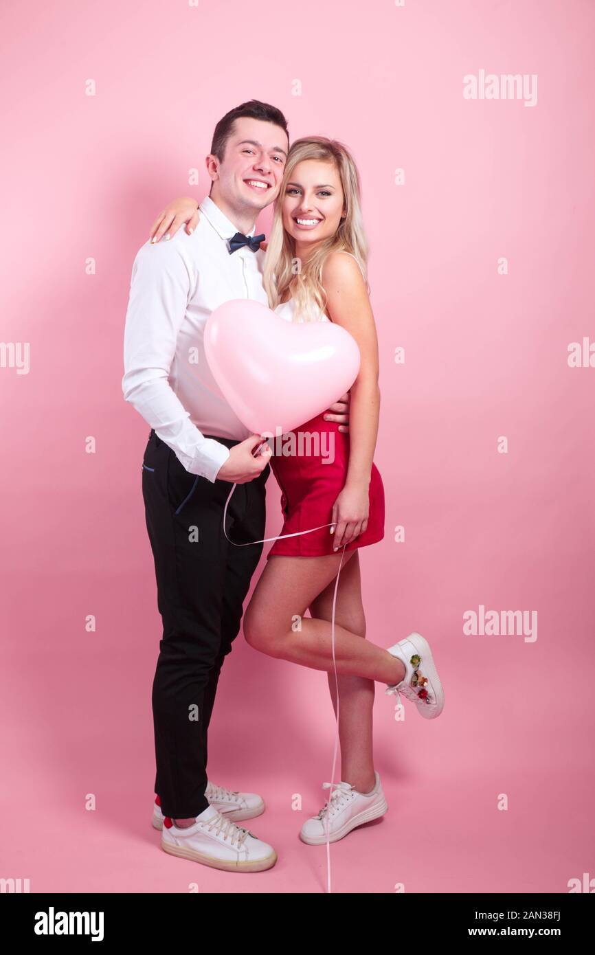 Happy couple posing on pink background with balloon heart. Valentine's ...