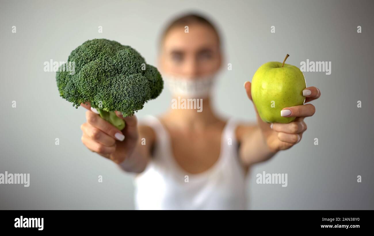 Anorexic model with taped mouth holding vegetables, concept of excessive fasting Stock Photo