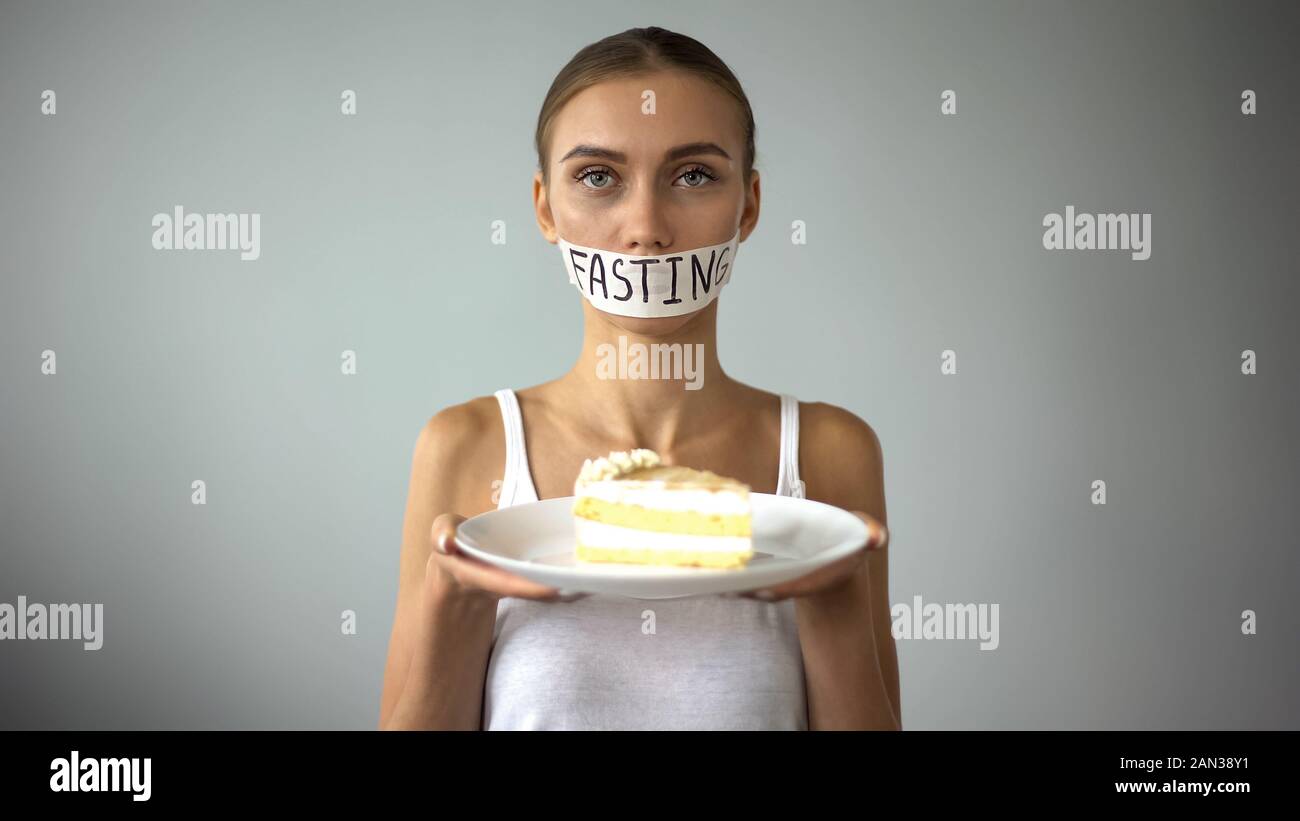 Anorexic girl holding pie, fasting word written on taped mouth, ban on sweets Stock Photo