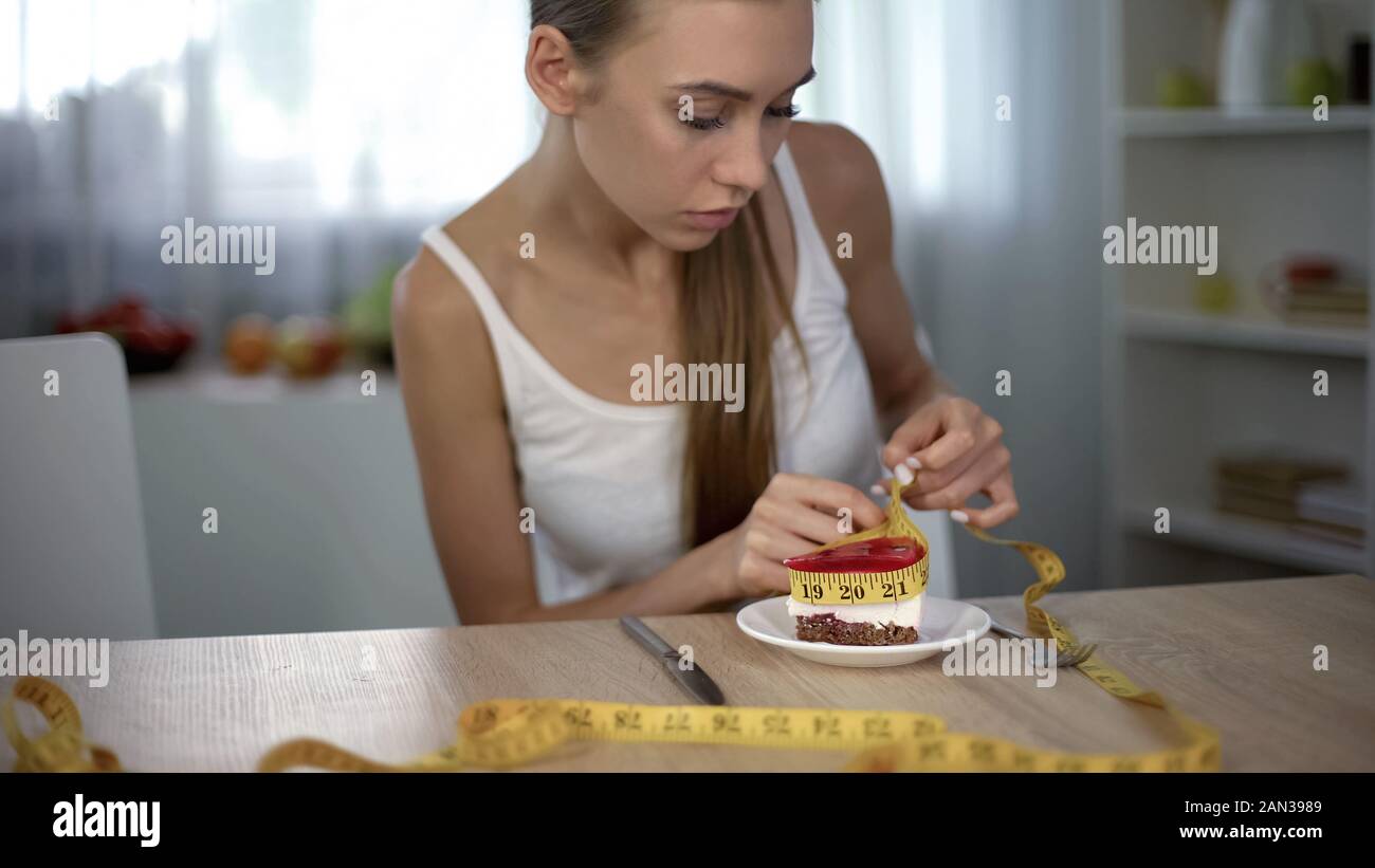 Underweight girl measuring piece of cake with tape, fear of gaining weight Stock Photo