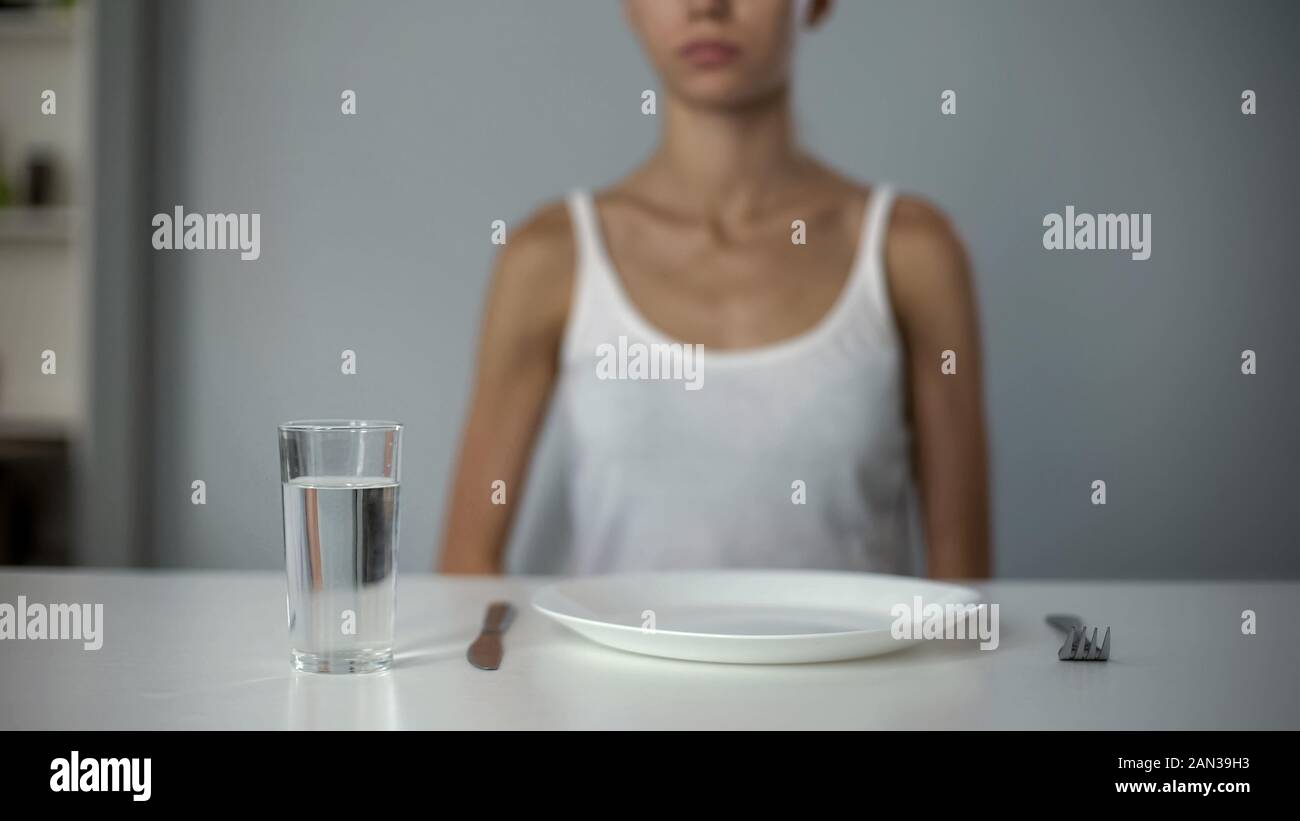 Anorexic girl sitting in front of empty plate, drinking water, severe diet Stock Photo