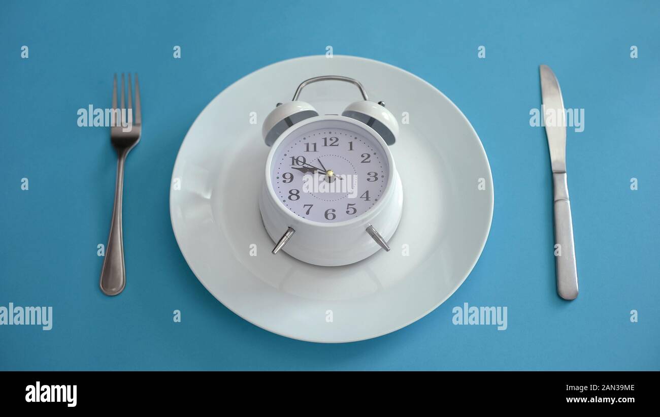 Alarm clock on plate, adhere to diet time, proper nutrition, discipline, closeup Stock Photo