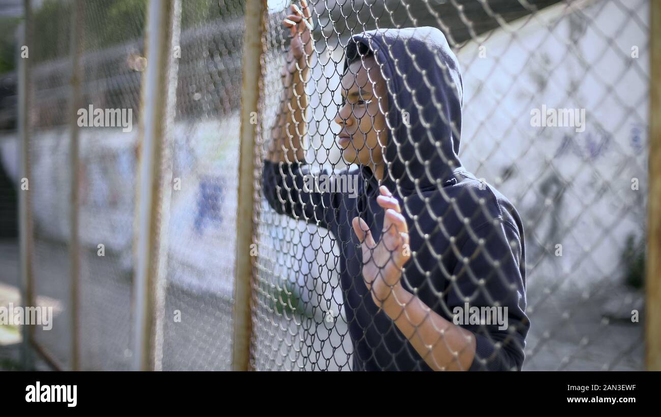 Afro-american boy behind metal fence, criminal in prison, dreaming about freedom Stock Photo