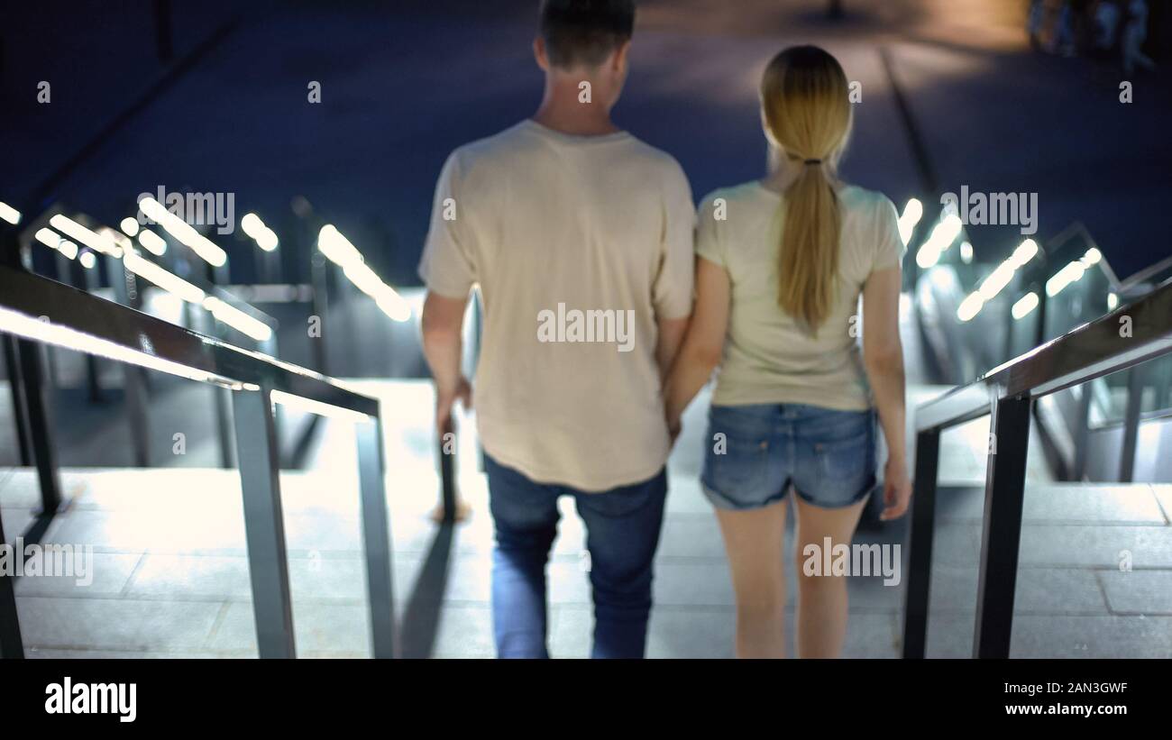 Young couple holding hands, walking downstairs in night city