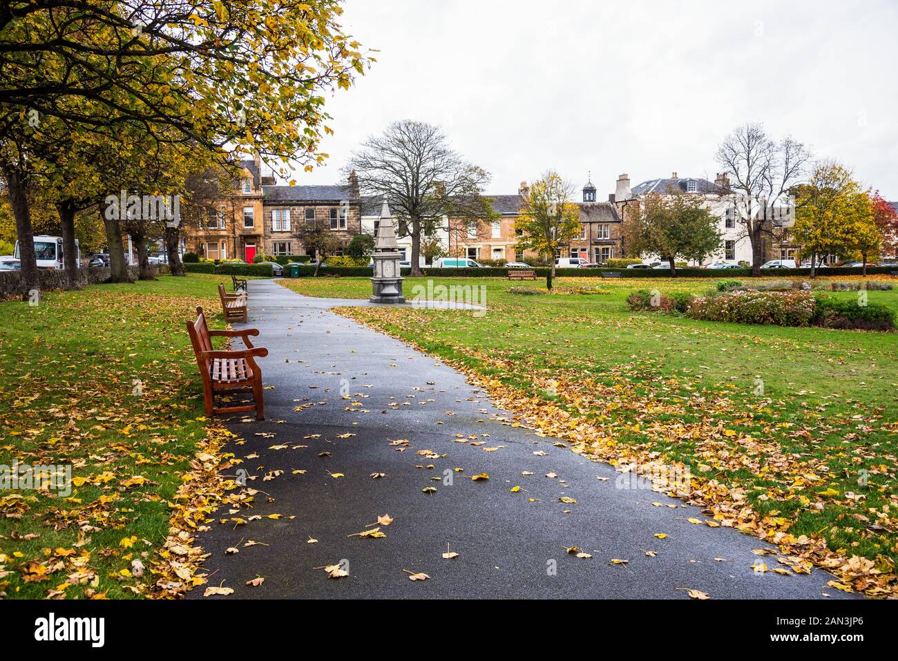 Garden with a path lined with wooden benches and deciduous trees in a residential district on a cloudy autumn day Stock Photo