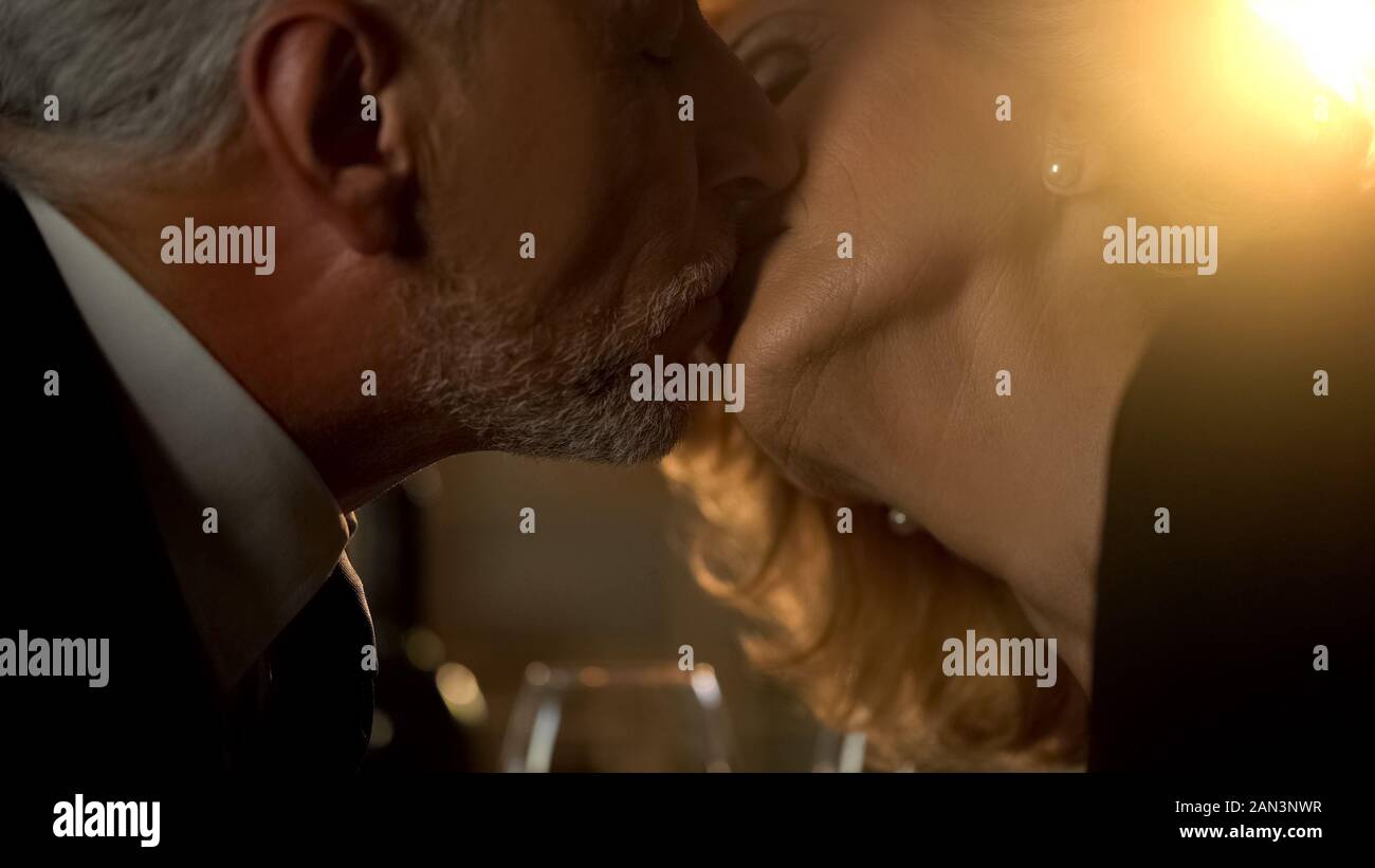 Loving elderly couple kissing in restaurant, aged grandparents on romantic date Stock Photo
