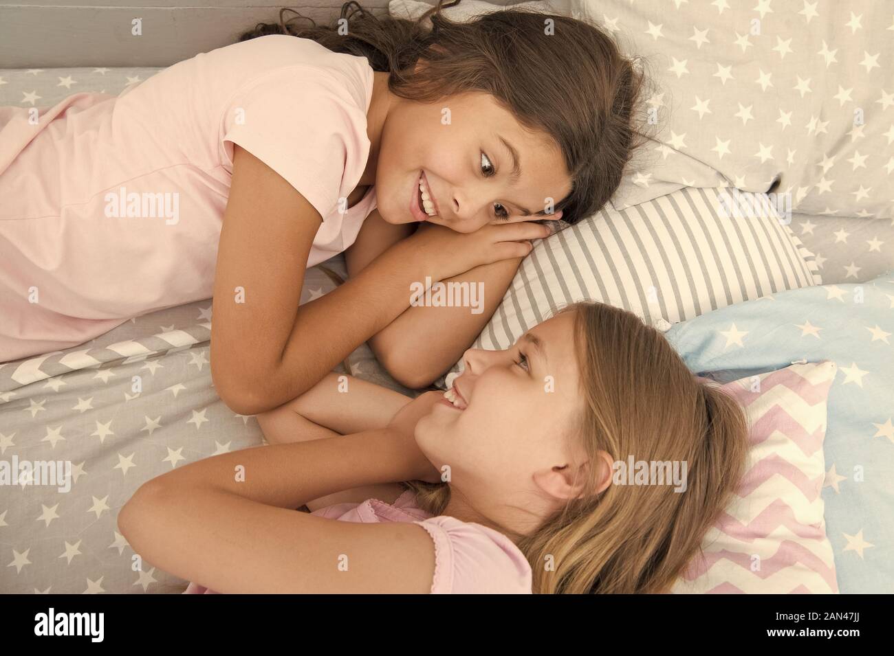 There is no friend than a sister. Happy little sisters talking during nap time. Small sisters relaxing in bed together. Adorable sisters or friends enjoying rest hour. Stock Photo
