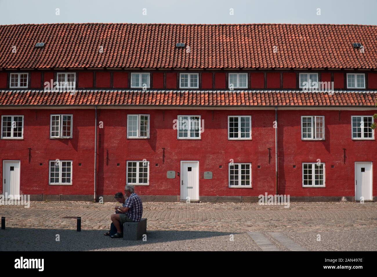People sit on a bench in front of houses on the island of Kastellet in Copenhagen, Denmark Stock Photo