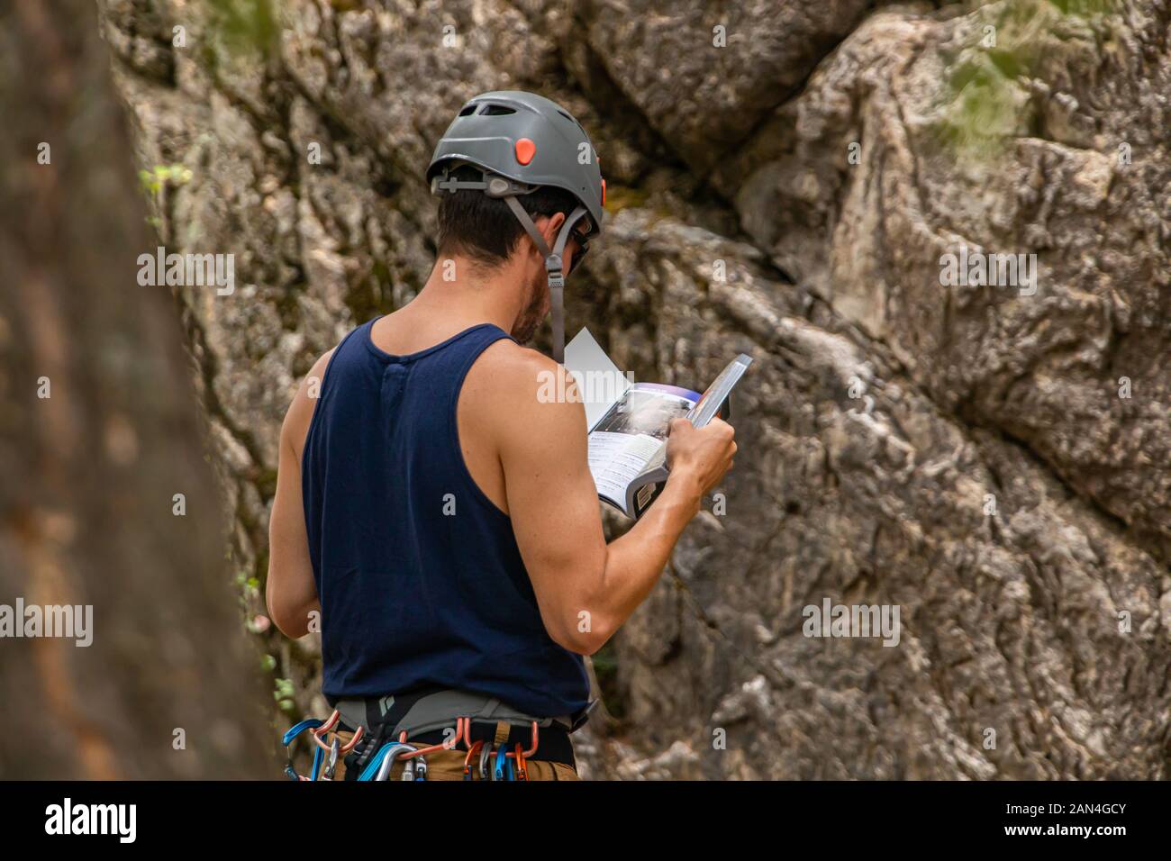 A masculine and healthy rock climber is seen from behind, reading an