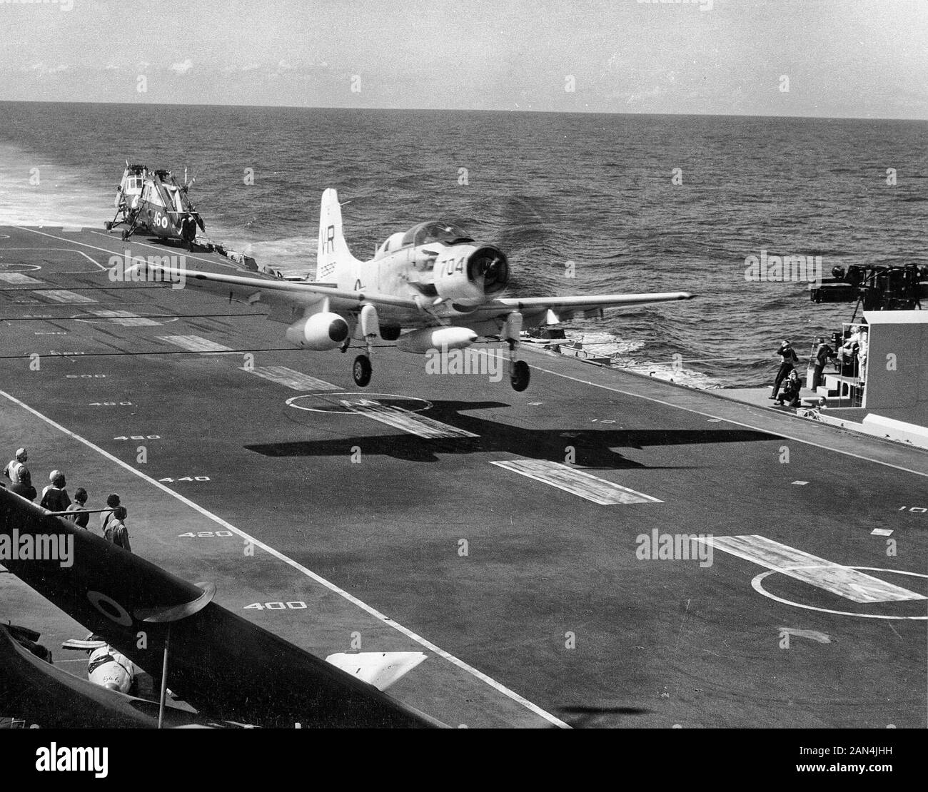 A U.S. Navy Douglas EA-1F Skyraider of electronic warfare squadron VAW-13 Zappers making a touch-and-go landing on the British aircraft carrier HMS Victorious (R38) off Cubi Point, Philippines, in late 1963 during a five-day exercise of U.S., British and Australian carriers. Note the two Westland Wessex helicopters parked on the fantail and the folded wings of a DeHavilland Sea Vixen fighter in the foreground. 1963 Stock Photo