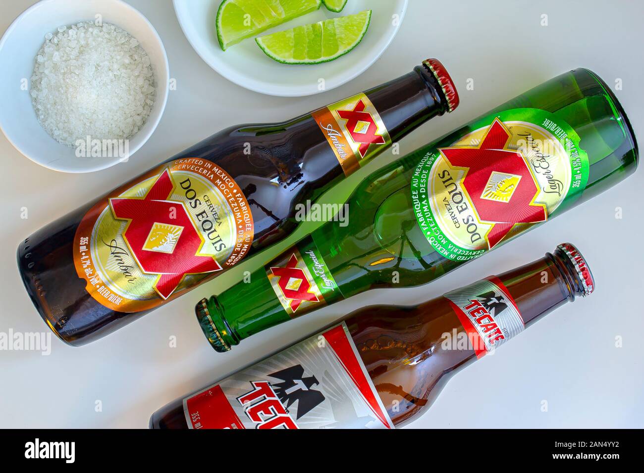 Bottles of Mexican pale and dark lager beers call: Tecate and Dos Equis on a white table with limes and salt on the side Stock Photo